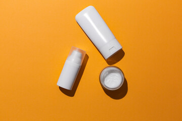 White blank cosmetic products bottles on orange background with free space for text, as advertisement.