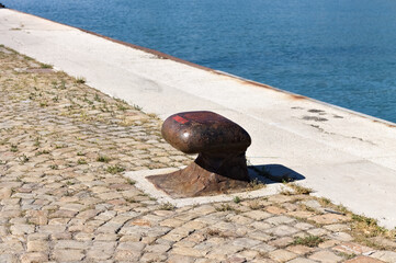 Isolated rusted mooring bollard on the jetty of a commercial dock (Pesaro, Italy, Europe)