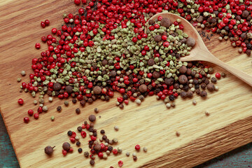 Assortment of scattered  spices in a spoon on a wooden board. Various types of red, black pepper and dried thyme seeds. Selective focus