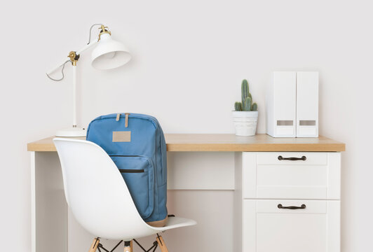 Wooden desk, supplies and school backpack on chair in room
