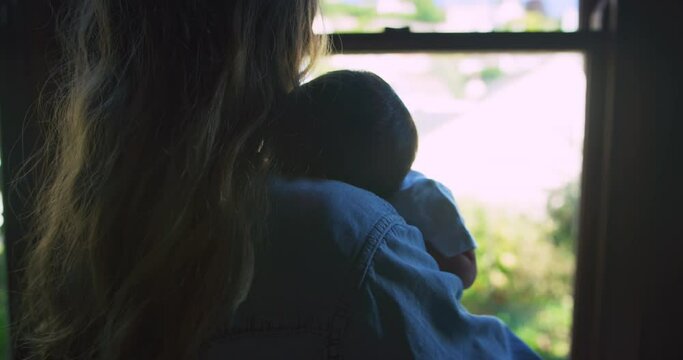 Young mother is holding her baby by the window at home