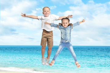 Cute school boy and girl jumping on beach near sea. Summer holidays