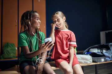 Sport kids girl before training listen music on phone in locker room.