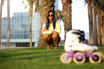 selective focus on a sporty young happy girl with blue hair and sunglasses sitting on the grass in...