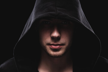 Close-up portrait of a courageous man in a deep dark hood on a black background. The concept of...