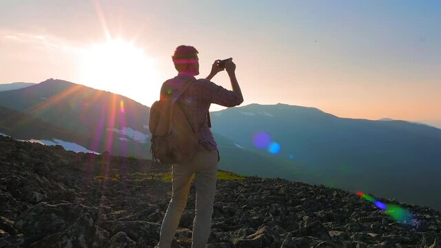 A man in the mountains photographs the landscape on his smartphone. A tourist with a backpack photographs the sunset on a mountain pass. Hiking in the mountains