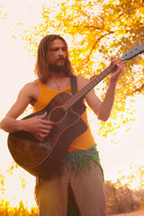 Hippie man playing an acoustic guitar in the autumn forest