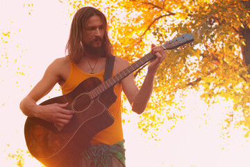 Hippie man playing an acoustic guitar in the autumn forest