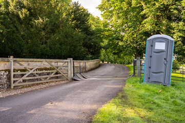 A plastic portable toilet next to a covered cattle grid on a public footpath in a field at an...