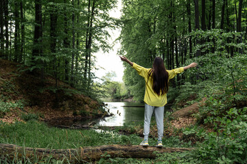 Naklejka na ściany i meble Young woman balances on a tree log near the lake