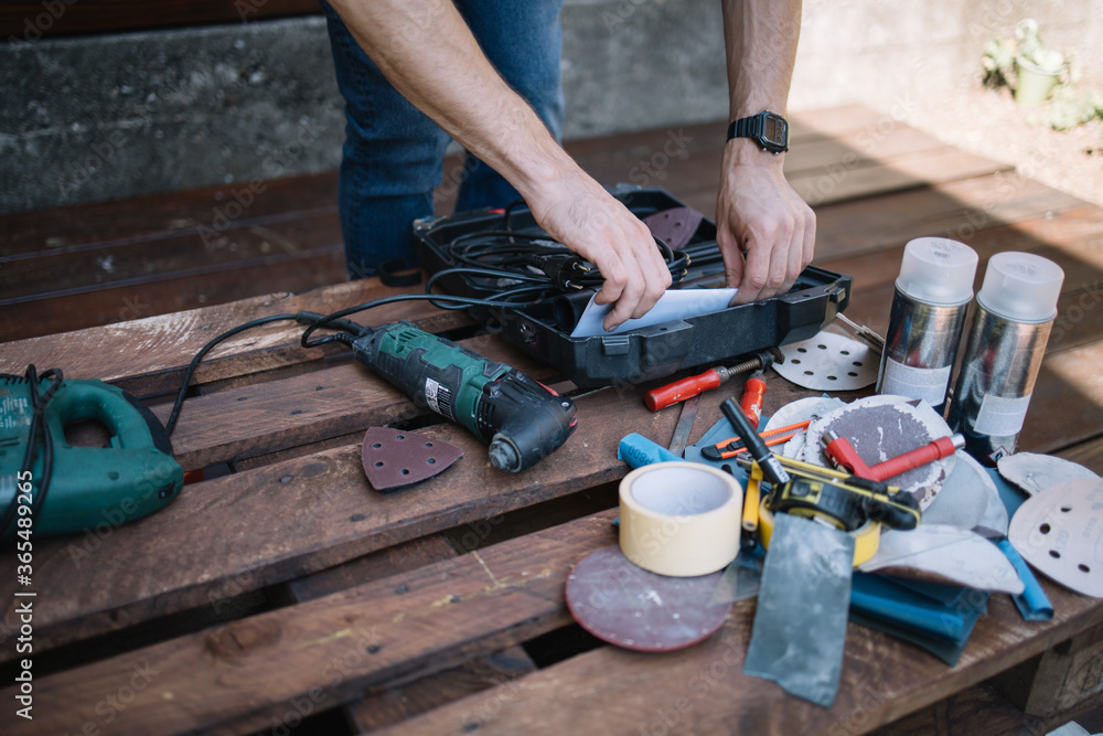 Wall mural Male hands opening a box on table with electric grinder. Man's hands over wooden table with electric saw and handyman tools.