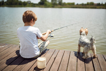 Boy having fun on fishing with his dog  in a pond.Summer joy on vacation.