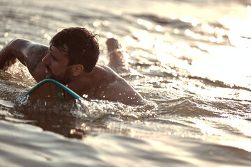 close up of young caucasian male surfer swimming on surfboard, catching the wave. copy space