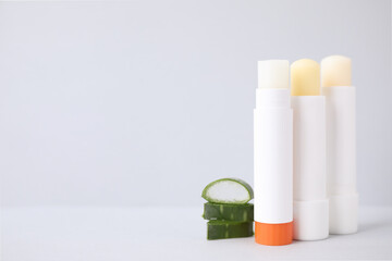 Hygienic lipsticks and cut aloe vera leaf on light table, space for text