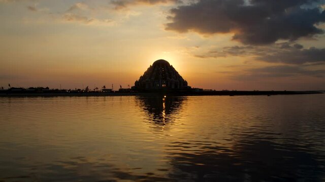 The sun setting behind the 99 domes mosque with a boat passing in the foreground