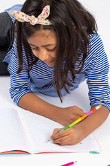 Cute left-handed girl is writing with a pencil in her notebook.