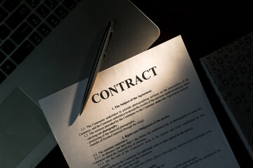Top view of laptop computer, contract, planner and silver pen on wooden table in office. Warm sunlight.