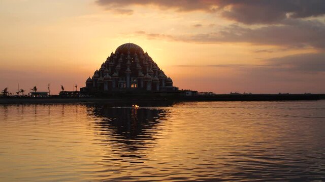The sun setting behind the 99 domes mosque with a boat passing in the foreground