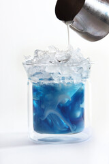Milk is poured into a glass with blue matcha tea. Vertical photo. Copy of the space. Light background.