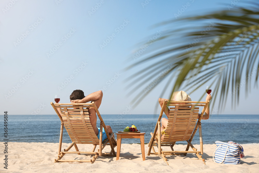 Poster couple with wine on sunny beach at resort