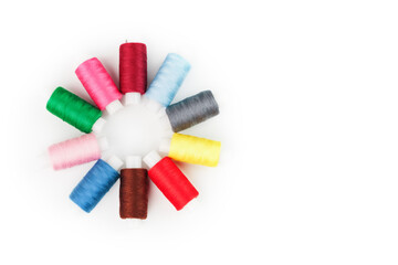 Sewing threads of different colors on reels on a white background in a circle.