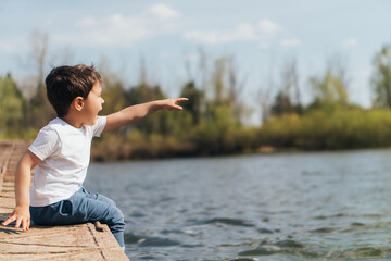 Profile of emotional boy pointing with finger while sitting near river