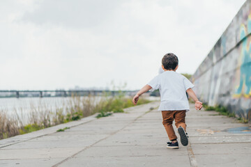 back view of boy in white t-shirt running outside