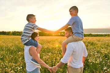 Happy family on daisy field at the sunset having great time together