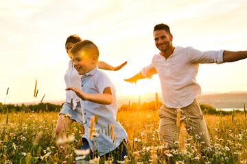 Happy family on daisy field at the sunset having great time together running and fly