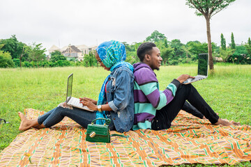 two young african friends sitting together in a park working together with their laptops