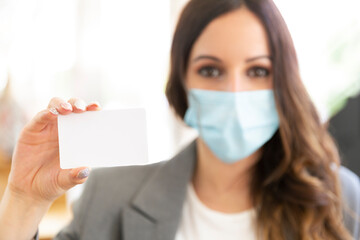 Female executive showing a blank credit card at the office. She's wearing a face mask and formal wear. Selective focus. Space for text. Business and new normal concept. 