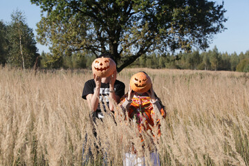Celebration of Halloween: people (couple is male, female) with jack-o'-lanterns in field with tree. Halloween decor from pumpkins. Autumn, fall nature. Halloween decoration. Halloween jack-o'-lanterns