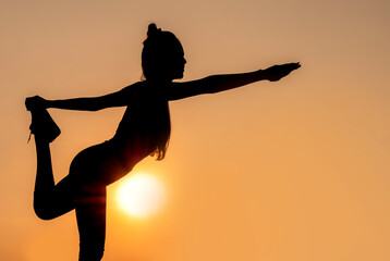 Silhouette of young woman doing yoga exercise during sunset