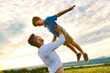 happy family of father and child on field at the sunset having fun flying in the air