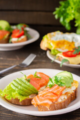 Different delicious sandwiches for breakfast, bread with cheese, avocado and trout, sandwich with egg, tomato and rucola, parsley