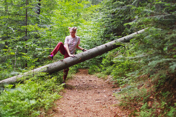 Naklejka na ściany i meble Young blonde woman near a large sawn log in a mountain forest.