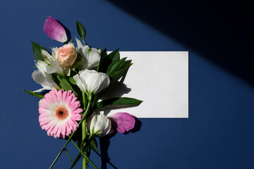 Beautiful bouquet of flowers. Bouquet of peonies, roses, gerberas with empty white paper a5 mock up isolated on a classic blue background. Flat lay, top view. Floral background. Add your text.