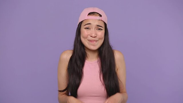 Fun confused shy shamed young asian woman girl 20s in pink clothes look camera bit lips spreading hands say oops i am sorry isolated on pastel purple violet background studio. People lifestyle concept