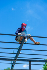 Worker welding the steel structure of roof with arc welding machine and blue sky in background