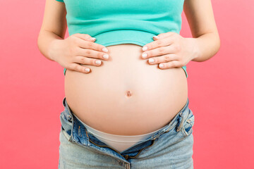 Close up of expecting mother in unzipped jeans showing her naked pregnant belly at colorful background with copy space. Pregnancy concept