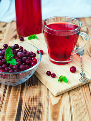 frozen cranberries with a mint leaf in a glass cup and fruit drink in a mug on a wooden table. Vertical photo