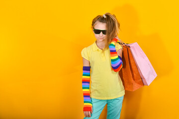 A girl with glasses stands with packages and poses on an orange background.