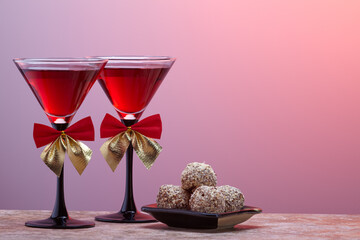 Two tall wineglasses with black stem decorated with bow ties, and chocolate handmade truffles.