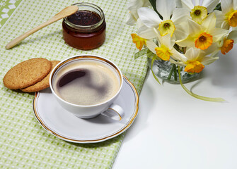 Coffee break. Cup of black coffee, cookies, marmalade and flowers on light background.