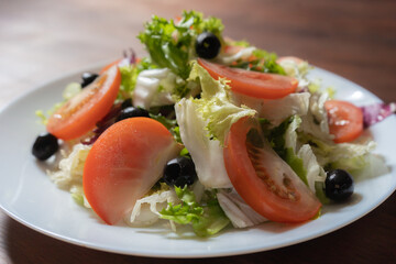 Fresh vegetable salad with tomatoes and olives. Colorful natural vitamin appetizer. Beautiful spring light meal or refreshment on white plate. Healthy food concept. Close up shot.
