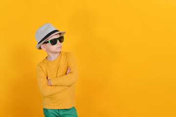 A boy in a gray hat and glasses posing on an orange background.