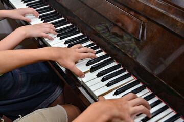 Top view of hands on piano keys playing the piano for four hands. Performance at a music institution.