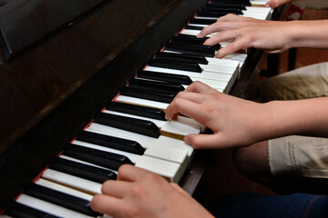 Brother and sister play the piano with four hands. Children learn the art of music.