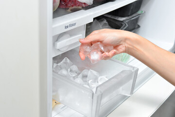 Woman with ice cubes from the freezer. An ice maker in a household refrigerator.