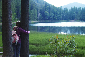 Young caucasian woman hugging a tree in the forest near the lake in summer evening.
